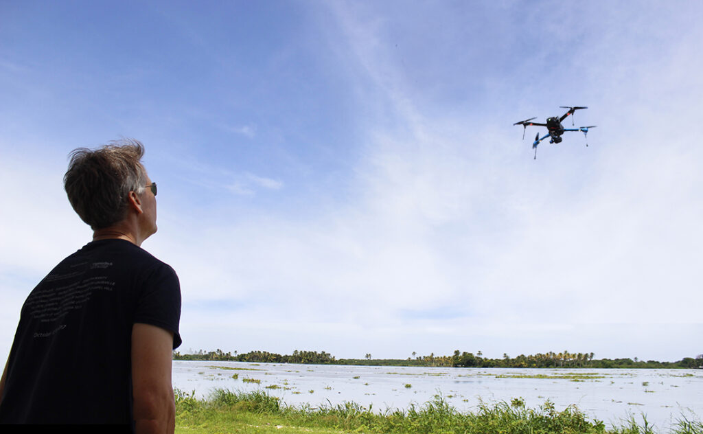 University of Miami Institute for Data Science and Computing, Software Engineering Director Chris Mader looking up at flying drone near riverbank