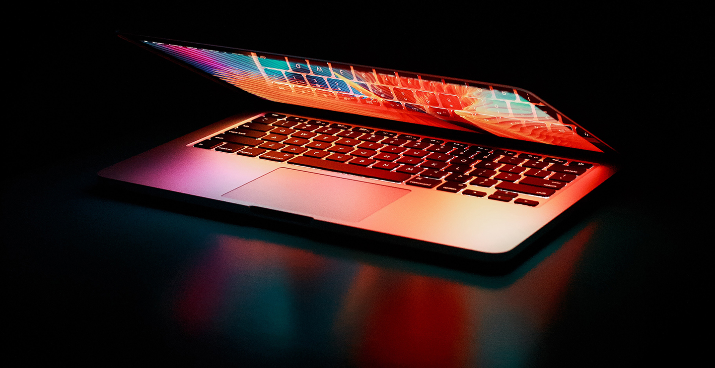 Pexels free image by Junior Teixeira, partially open laptop showing shades of hot pink, turquoise, red, and orange in the reflection of the keyboard on the screen and on the black shiny tabletop